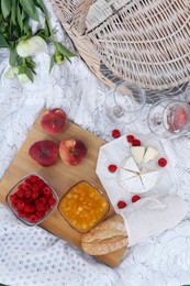 White picnic blanket with tasty food, flowers and basket, flat lay