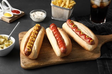 Photo of Fresh delicious hot dogs with sauces served on black table