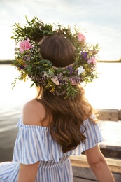 Photo of Young woman wearing wreath made of beautiful flowers on pier near river