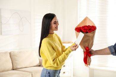 Photo of Happy woman receiving red tulip bouquet and greeting card from man at home. 8th of March celebration