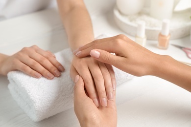 Cosmetologist massaging client's hand at table in spa salon, closeup