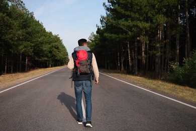 Man with backpack going along road near forest, back view