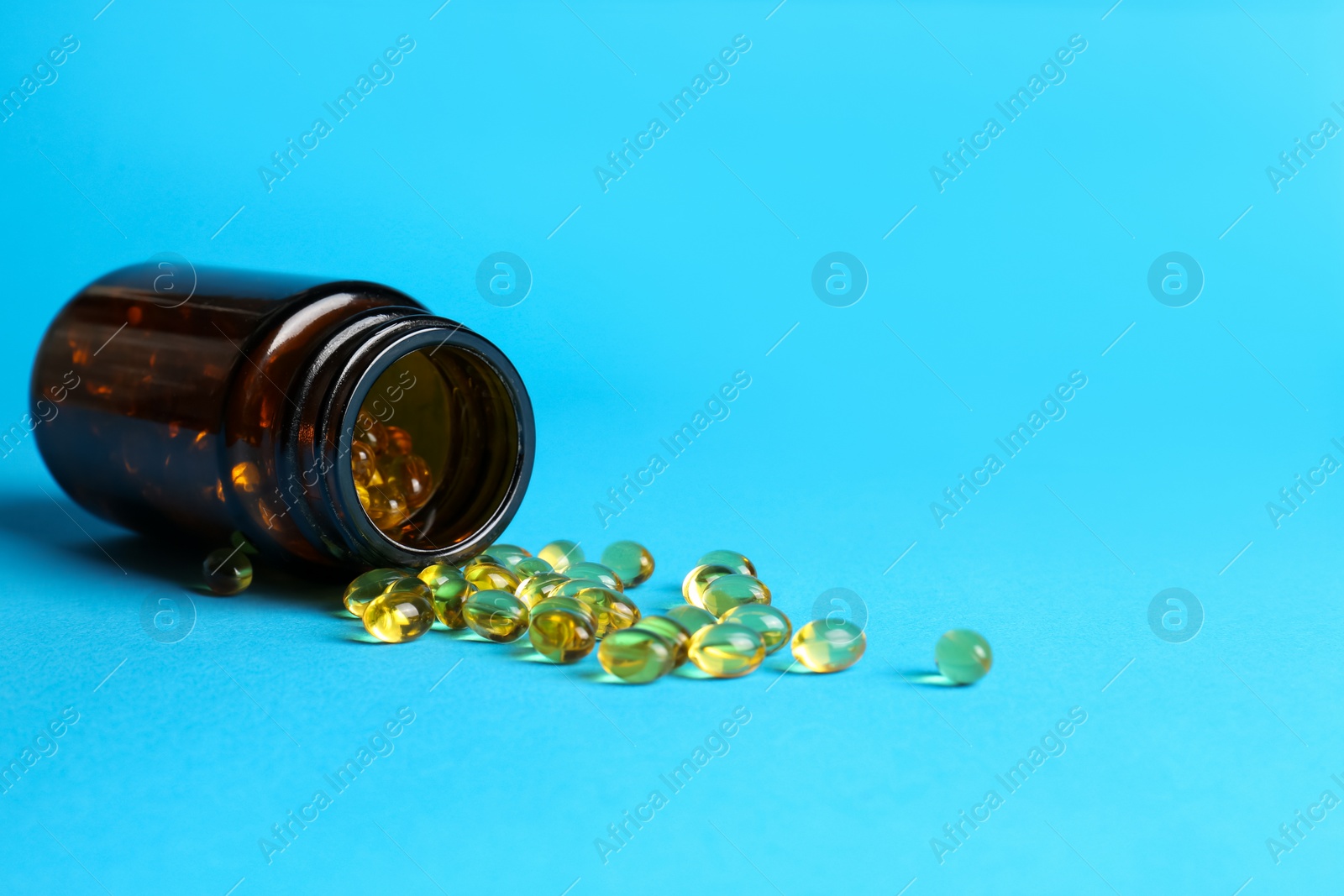 Photo of Medical bottle and yellow capsules on light blue background, space for text