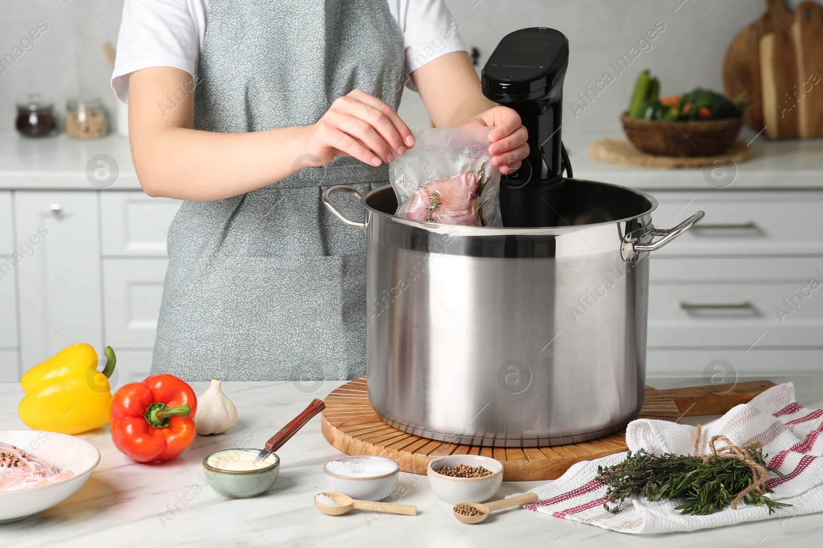 Photo of Woman putting vacuum packed meat into pot in kitchen, closeup. Thermal immersion circulator for sous vide cooking