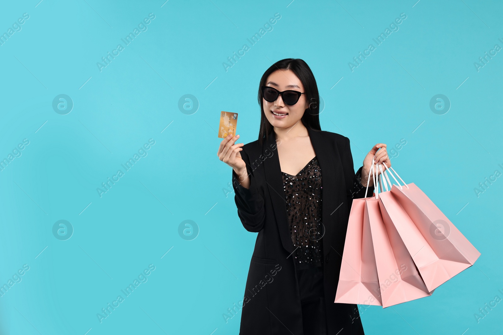 Photo of Smiling woman with shopping bags and credit card on light blue background. Space for text