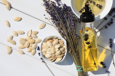 Photo of Healthy cooking oil, lavender flowers and pumpkin seeds on white wooden table, closeup