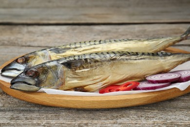 Photo of Delicious smoked mackerels, chili pepper and onion on wooden table, closeup