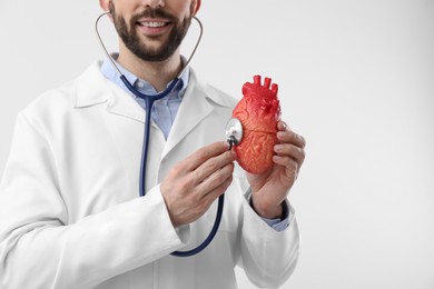 Photo of Doctor with stethoscope and model of heart on white background, closeup. Cardiology concept