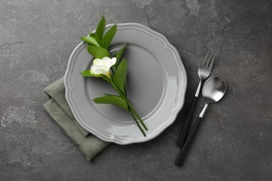 Photo of Stylish setting with cutlery, napkin, flower and plate on grey textured table, flat lay
