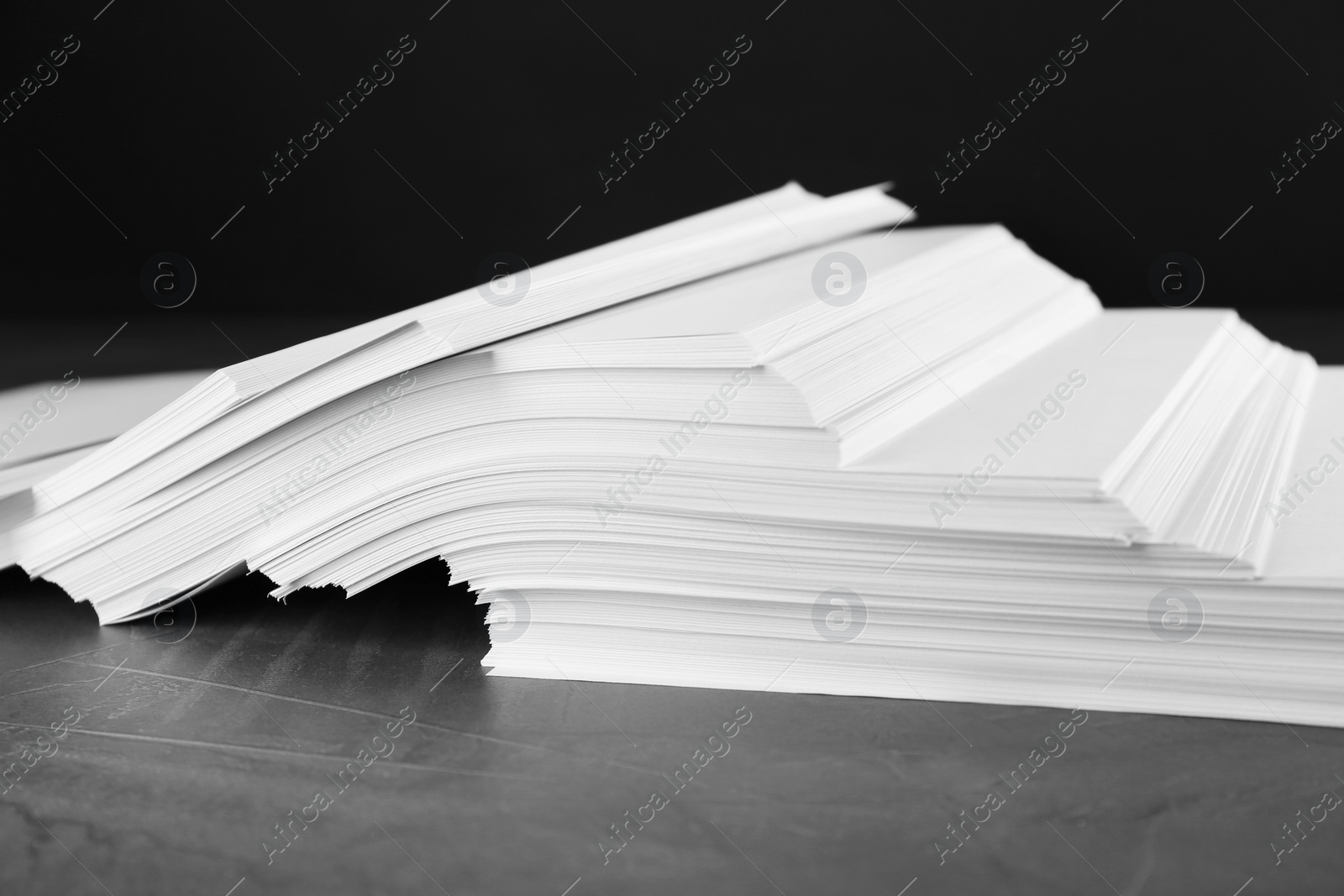 Photo of Stack of blank paper on grey stone table against black background