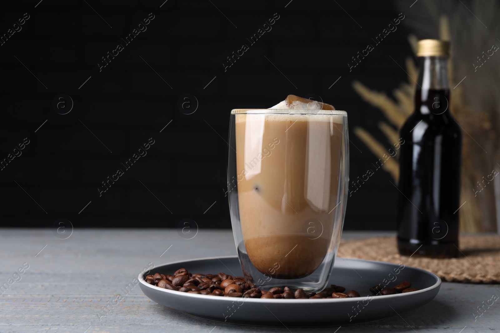 Photo of Glass of coffee with syrup and beans on light grey table. Space for text