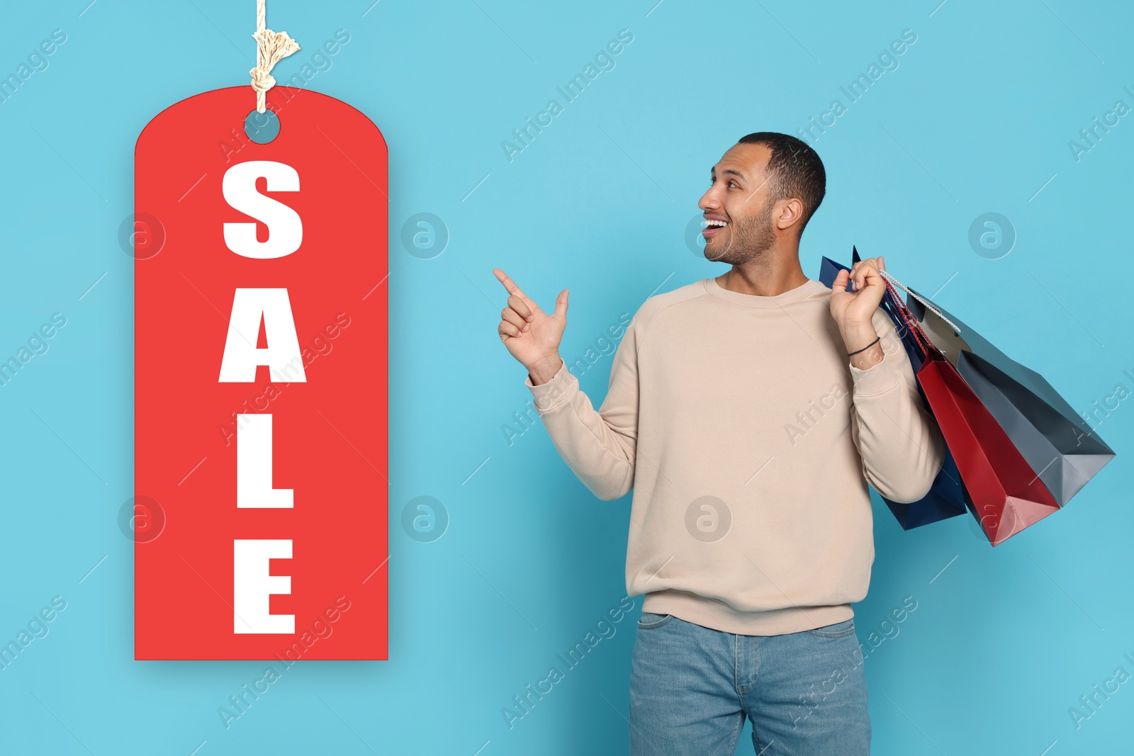 Image of Happy man with shopping bags pointing at Sale label on light blue background