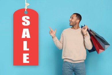 Image of Happy man with shopping bags pointing at Sale label on light blue background