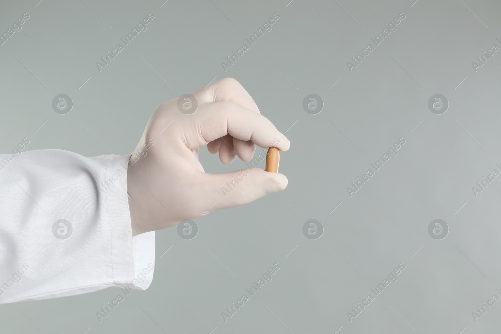 Photo of Doctor holding suppository for hemorrhoid treatment on light grey background, closeup