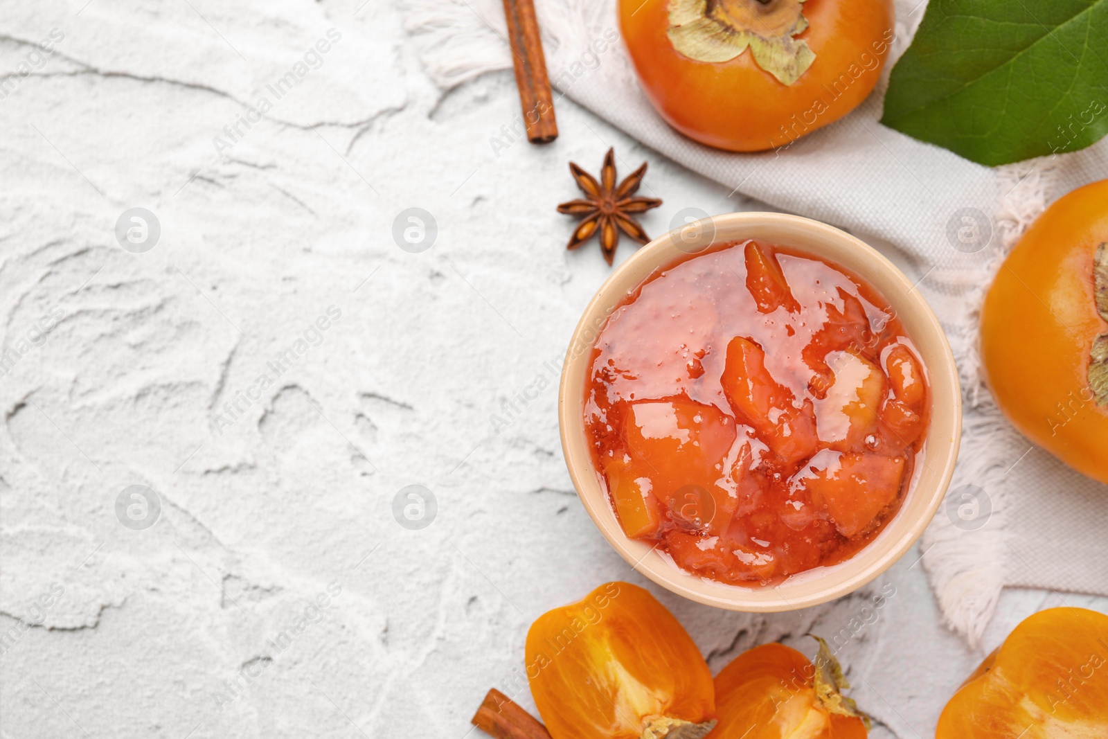 Photo of Bowl of tasty persimmon jam and ingredients on white textured table, flat lay. Space for text