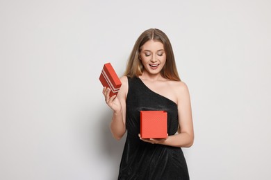 Photo of Emotional young woman in elegant black dress opening red gift box on white background