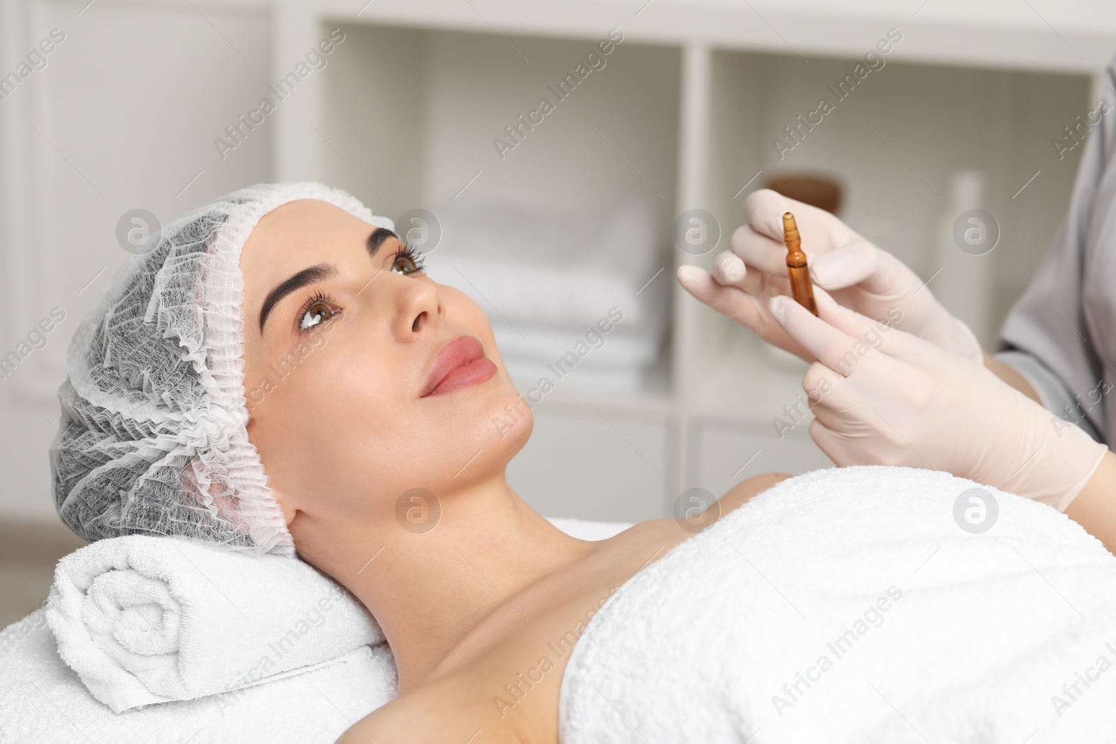 Photo of Professional cosmetologist holding skincare ampoule while working with client in clinic, closeup