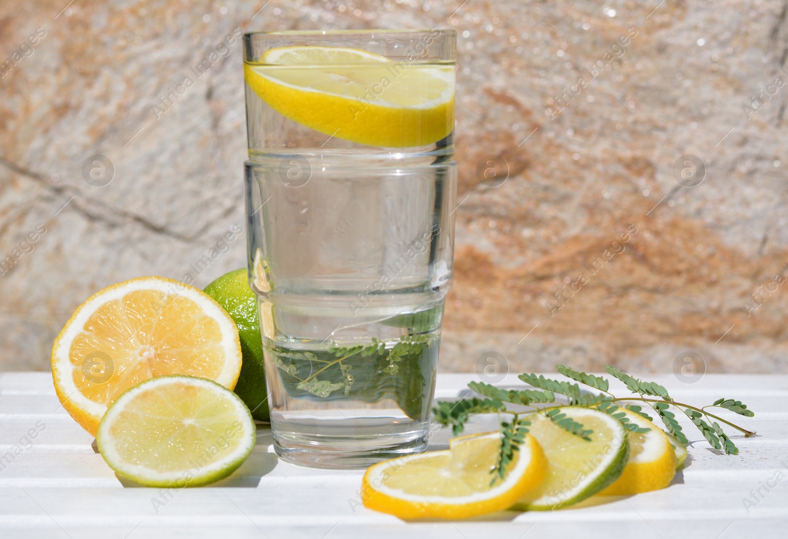 Photo of Delicious refreshing lemonade and pieces of citrus on white wooden table outdoors