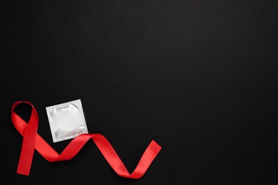 Red ribbon and condom on black background, flat lay with space for text. AIDS disease awareness