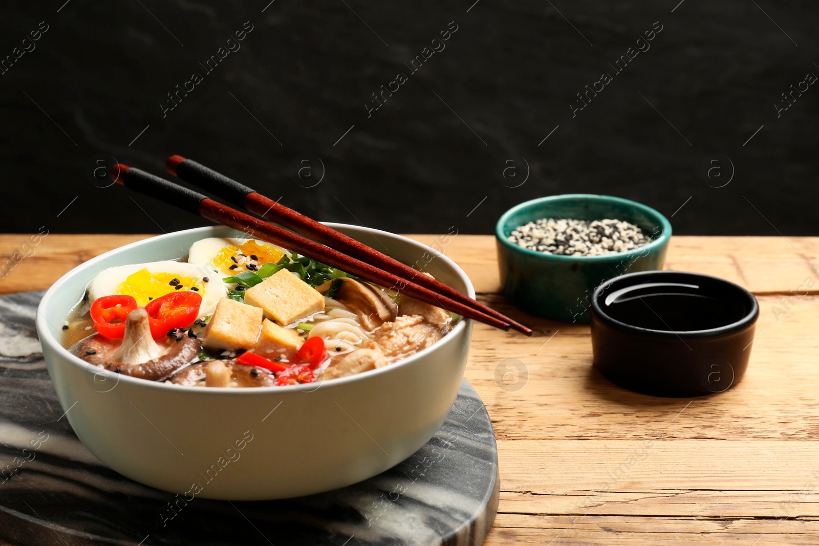 Photo of Noodle soup. Bowl of delicious ramen and chopsticks on wooden table, closeup