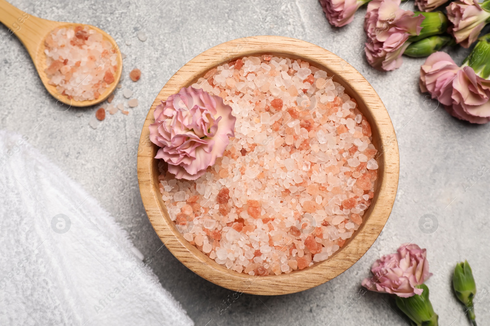 Photo of Bowl with natural sea salt, spoon and beautiful flowers on light grey table, flat lay