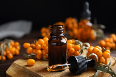 Photo of Ripe sea buckthorn and essential oil on wooden board against black background