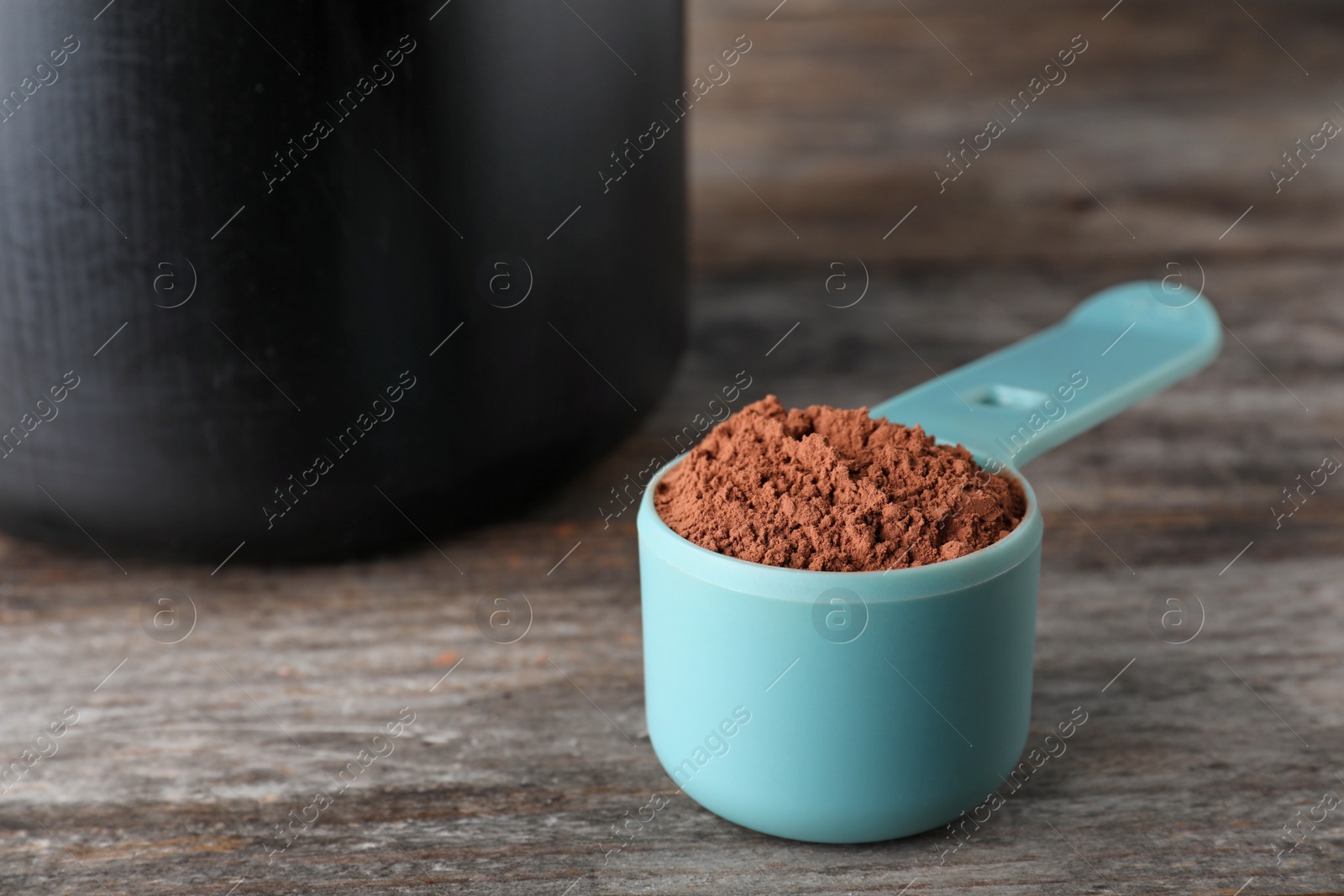 Photo of Scoop of chocolate protein powder on wooden table, space for text