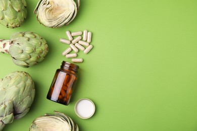 Photo of Bottle with pills and fresh artichokes on light green background, flat lay. Space for text