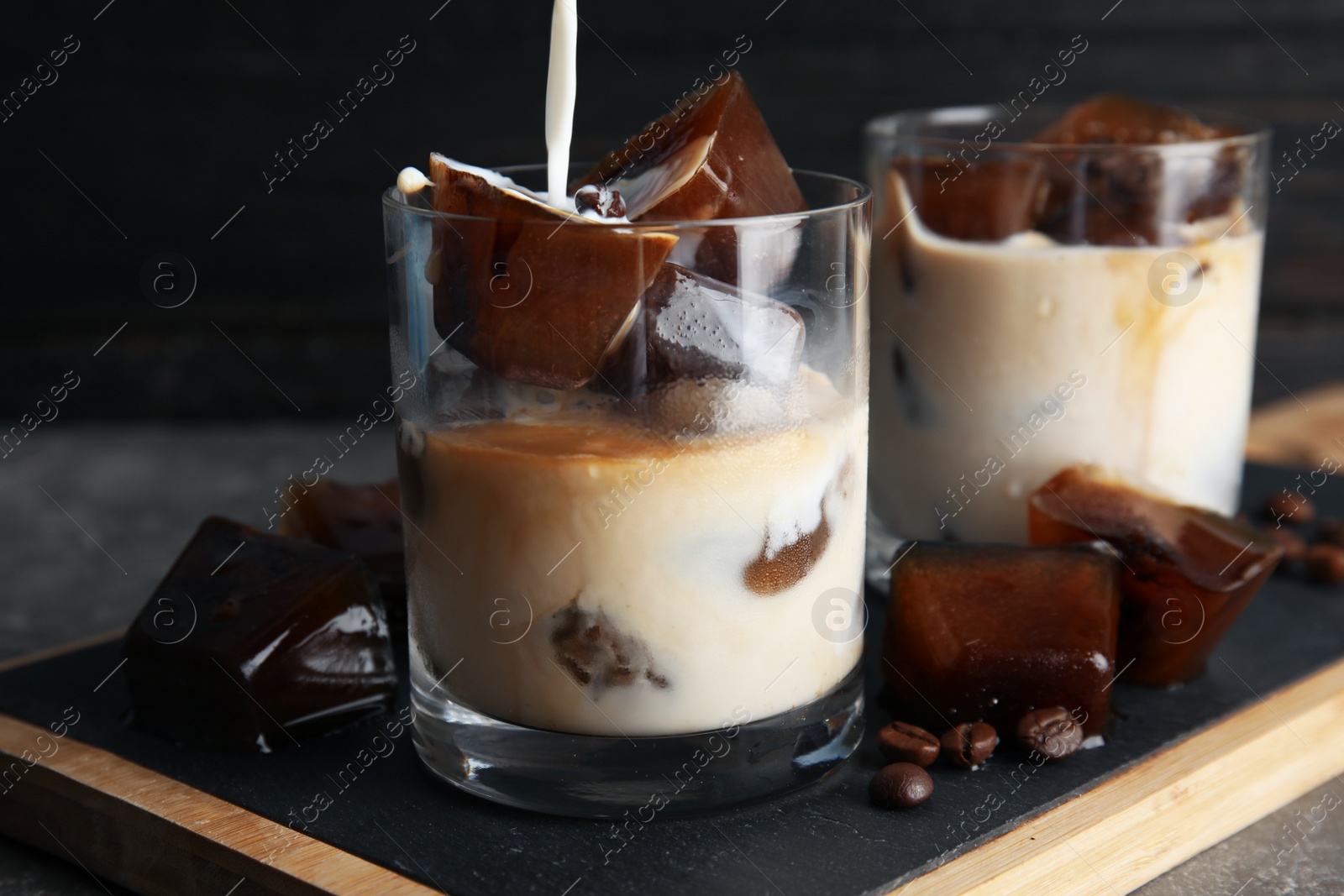 Photo of Pouring milk into glass with coffee ice cubes on table