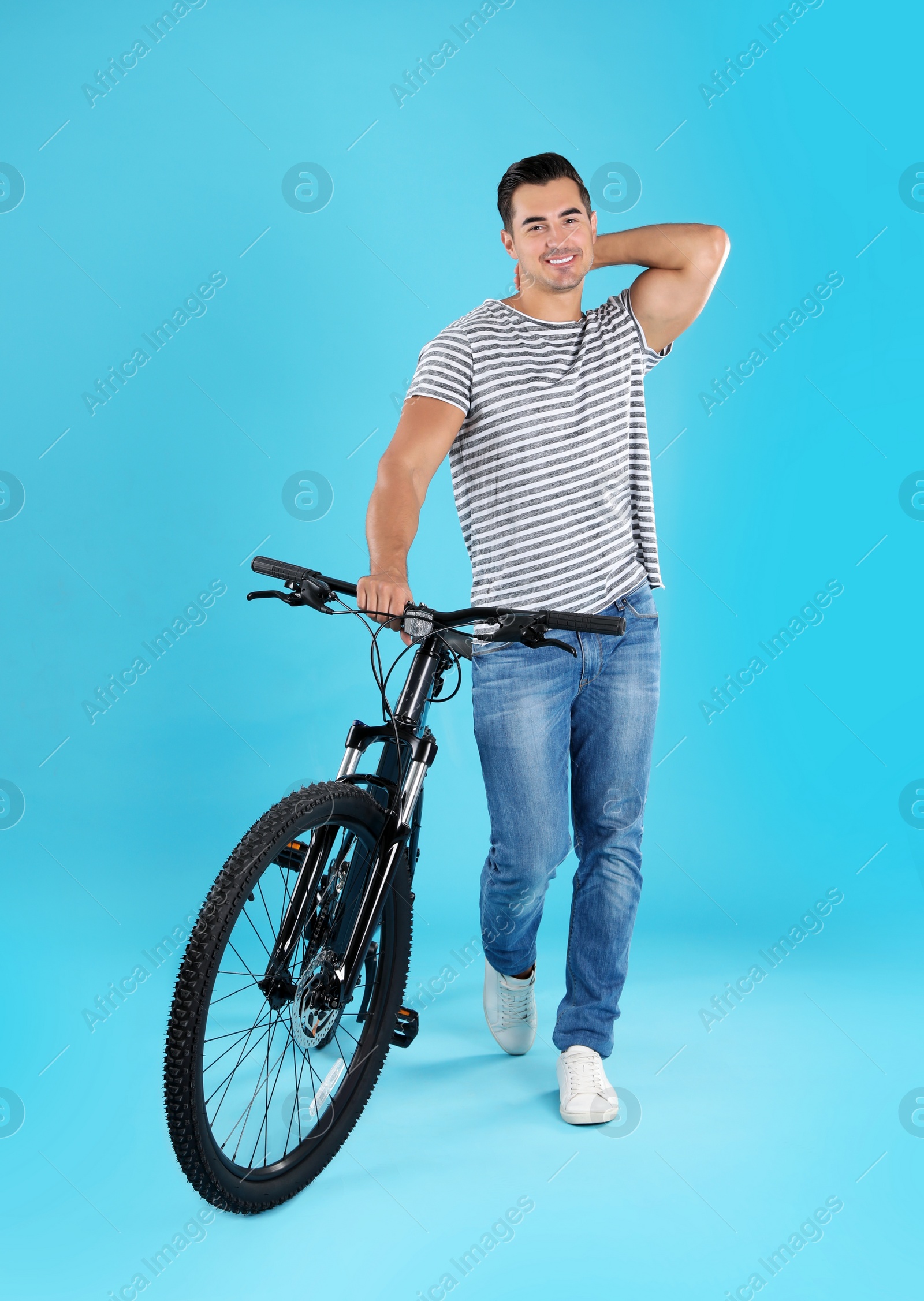 Photo of Handsome young man with modern bicycle on light blue background