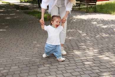 Photo of Mother supporting happy daughter while she learning to walk outdoors, closeup