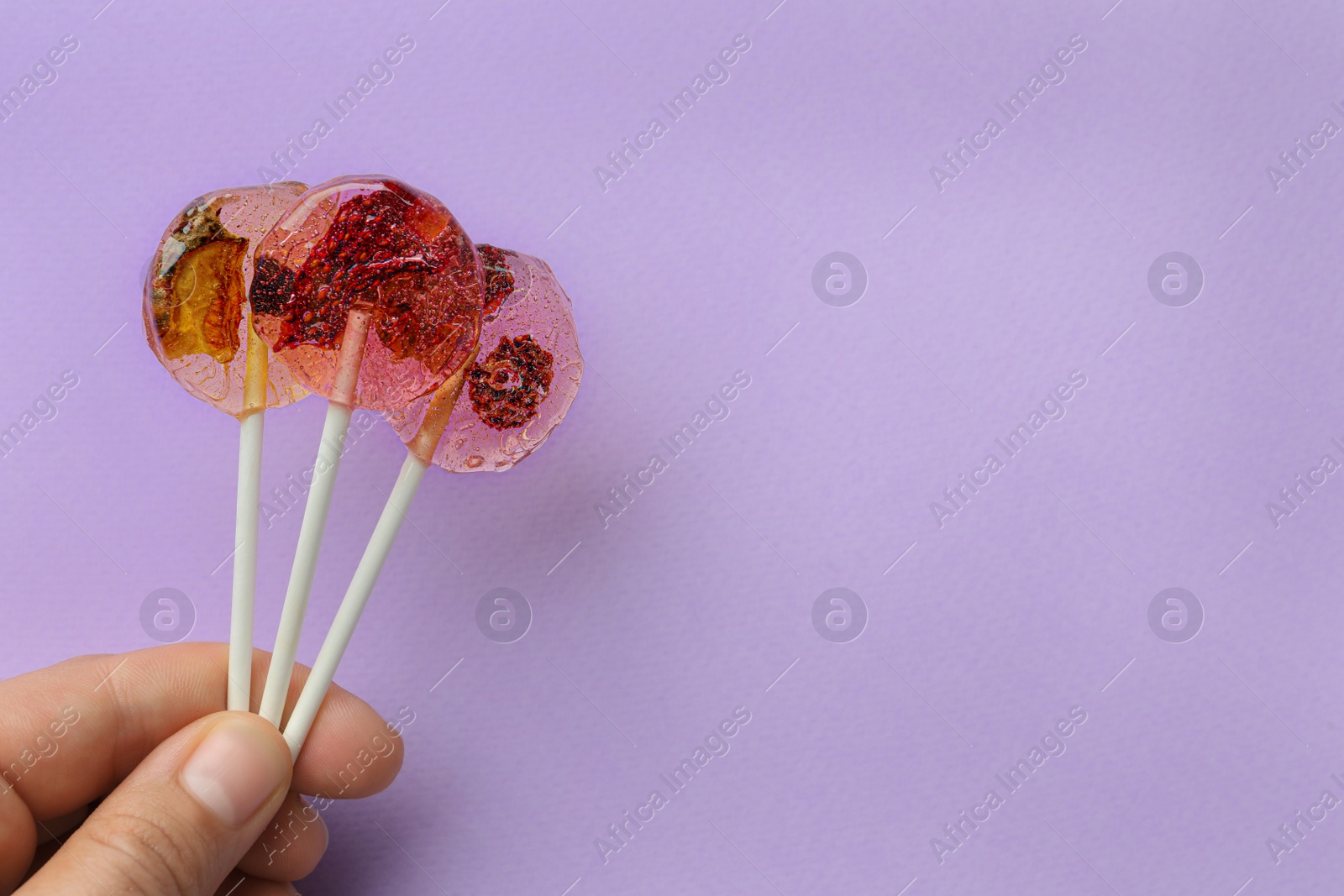 Photo of Woman holding sweet colorful lollipops with berries on lilac background, closeup. Space for text