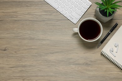 Photo of Computer keyboard, green houseplant, cup of drink and different stationery on wooden desk, flat lay with space for text. Home office