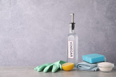 Photo of Natural cleaning products. Vinegar in bottle, baking soda, lemon, glove and sponge on light grey table. Space for text