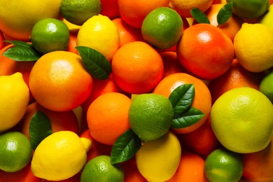 Photo of Different fresh citrus fruits and leaves as background, top view