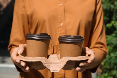 Photo of Woman holding takeaway cardboard coffee cups with plastic lids outdoors, closeup