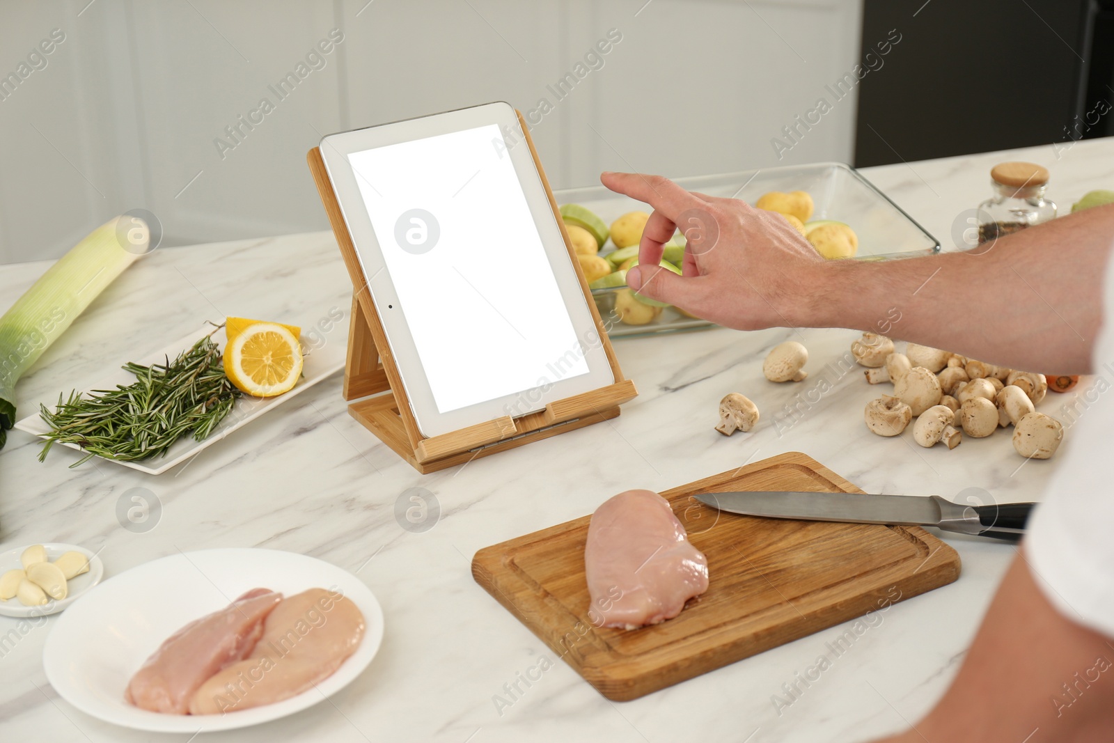 Photo of Man making dinner while watching online cooking course via tablet in kitchen, closeup