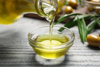Photo of Pouring olive oil into bowl on wooden table, closeup. Healthy cooking