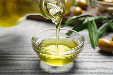 Pouring olive oil into bowl on wooden table, closeup. Healthy cooking