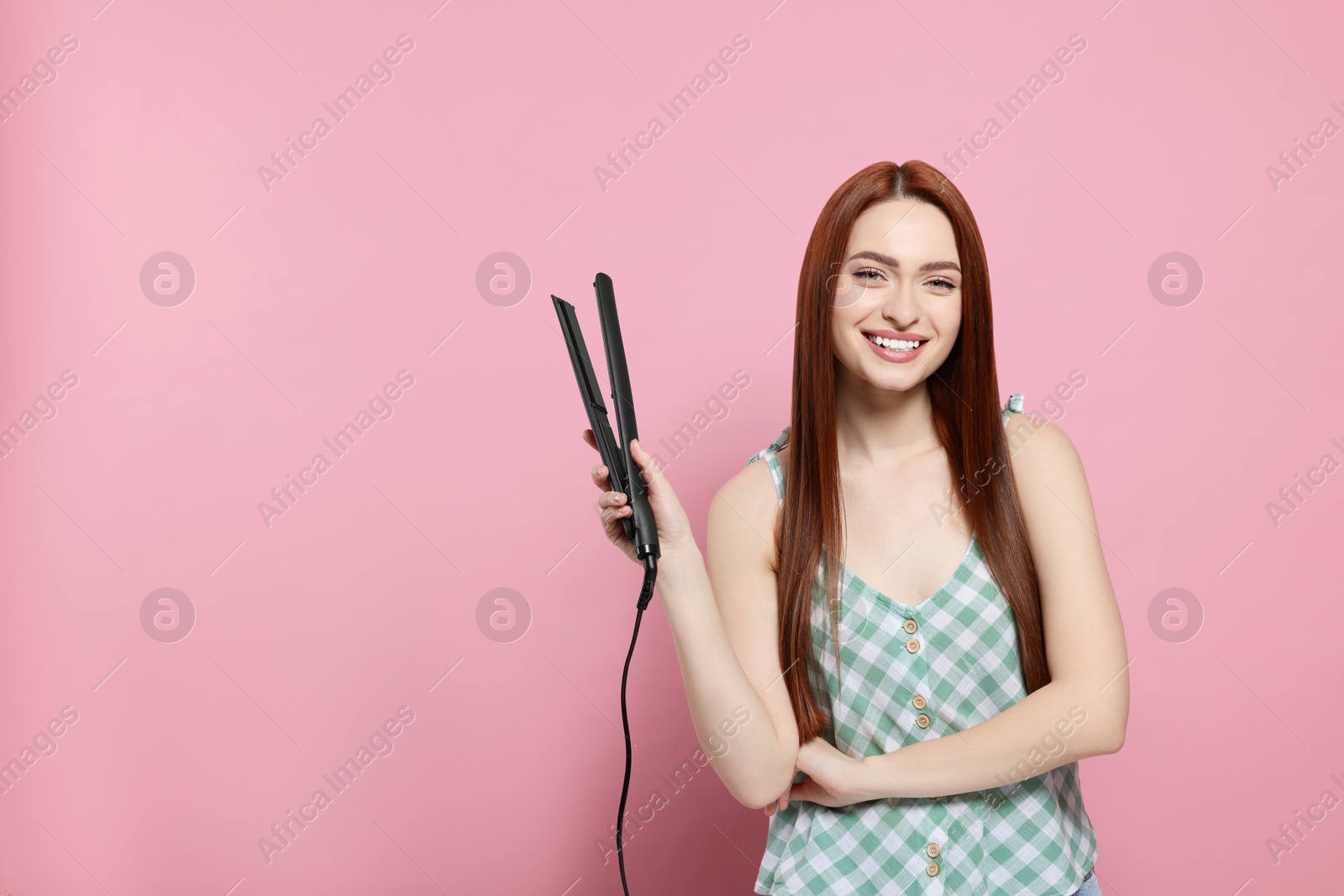 Photo of Beautiful woman with hair iron on pink background, space for text