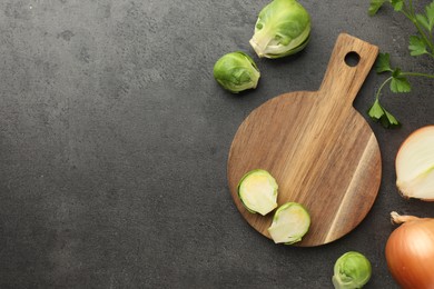 Photo of Wooden cutting board, Brussels sprouts, onion and parsley on dark textured table, flat lay. Space for text