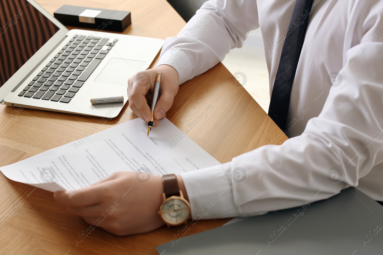 Photo of Notary signing document at wooden table, closeup