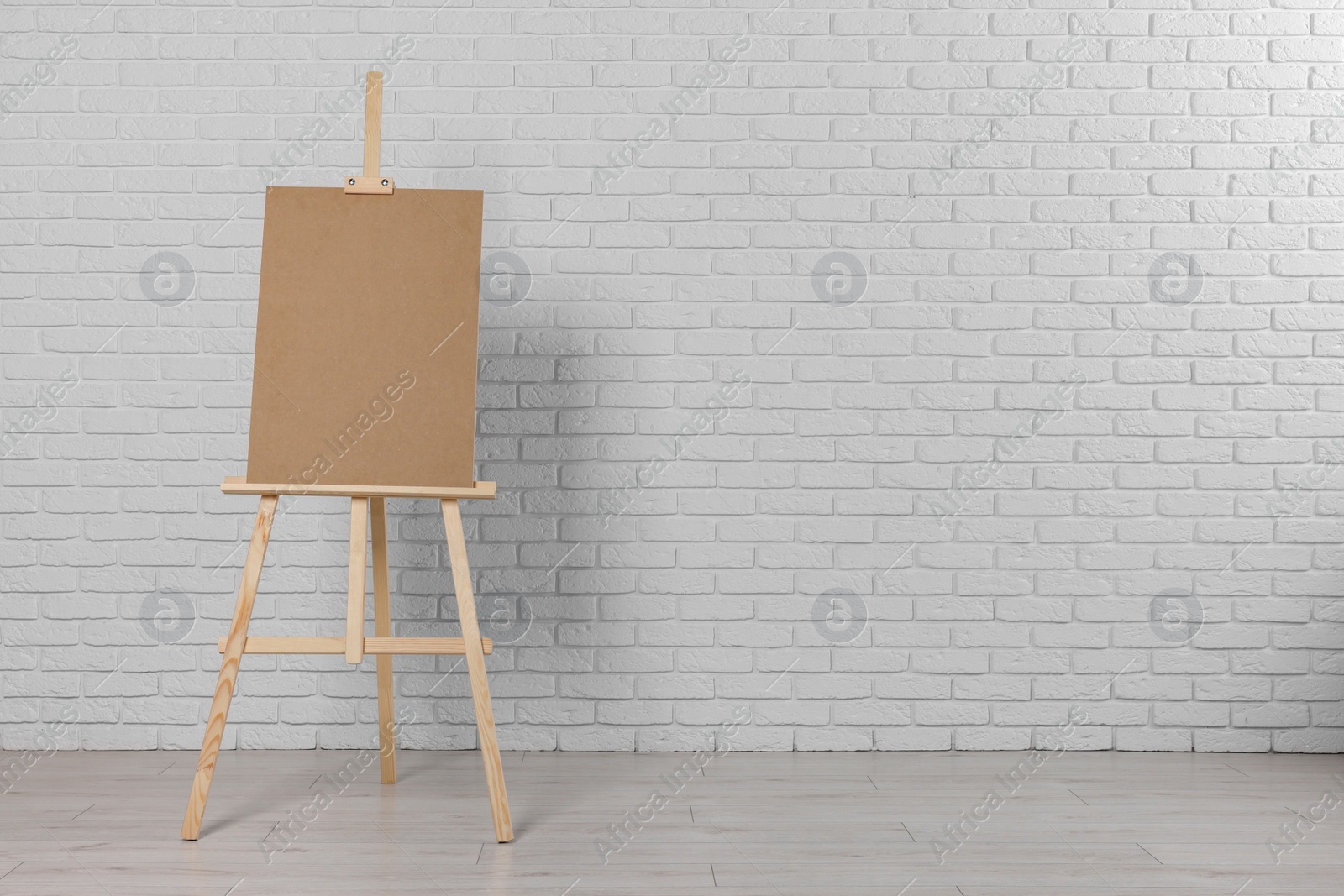 Photo of Wooden easel with blank board near white brick wall indoors. Space for text