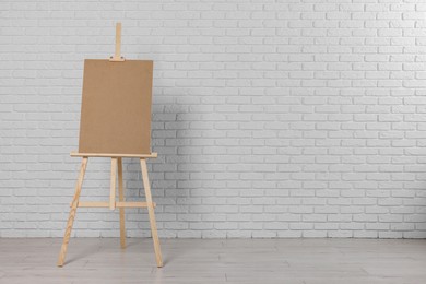 Photo of Wooden easel with blank board near white brick wall indoors. Space for text