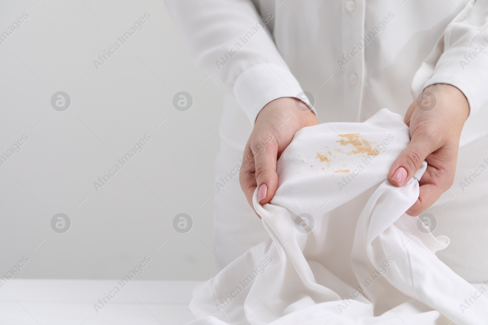 Photo of Woman holding shirt with stain against light background, closeup. Space for text