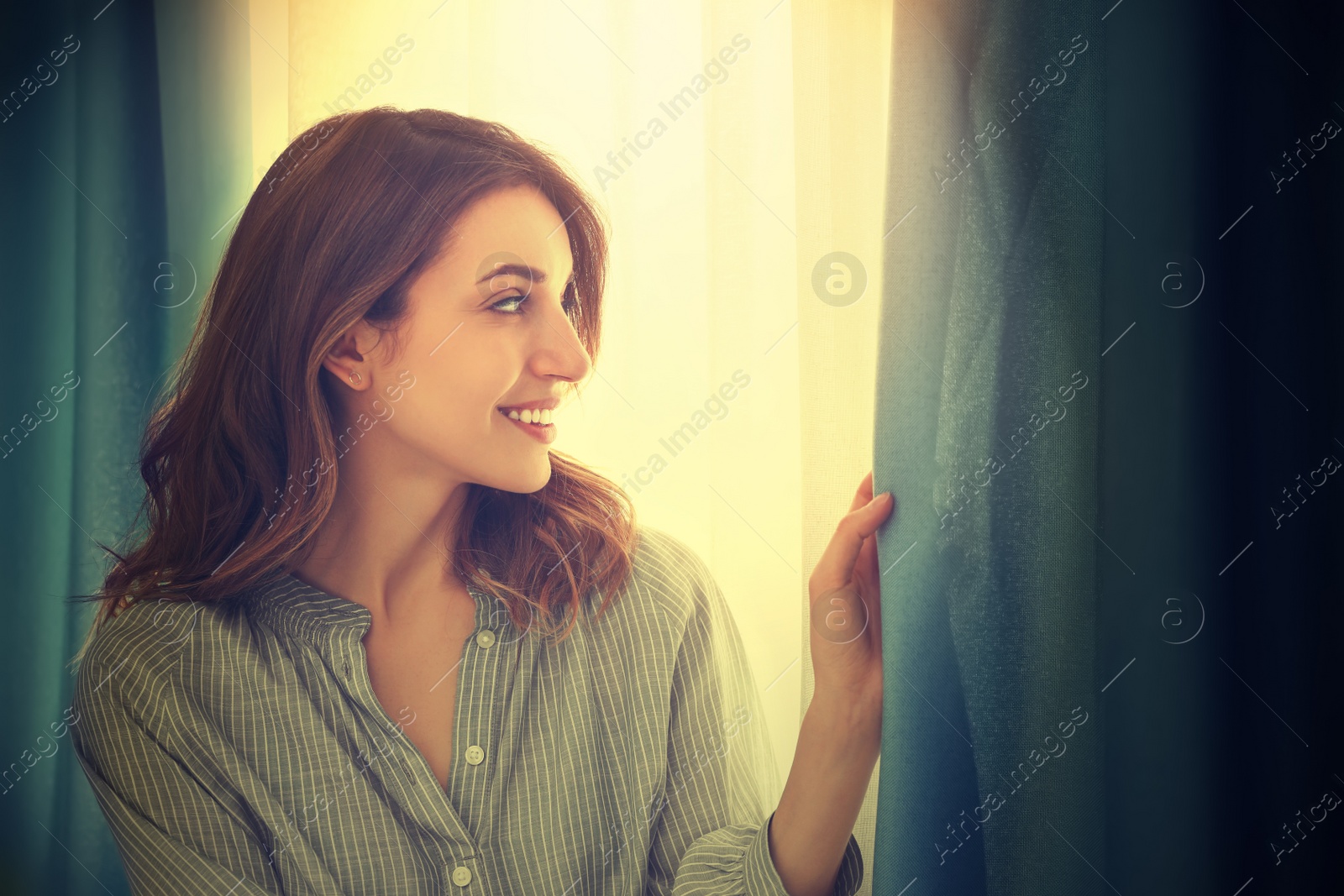 Image of Happy woman opening window curtains at home