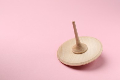 Photo of One wooden spinning top on pink background, closeup. Space for text