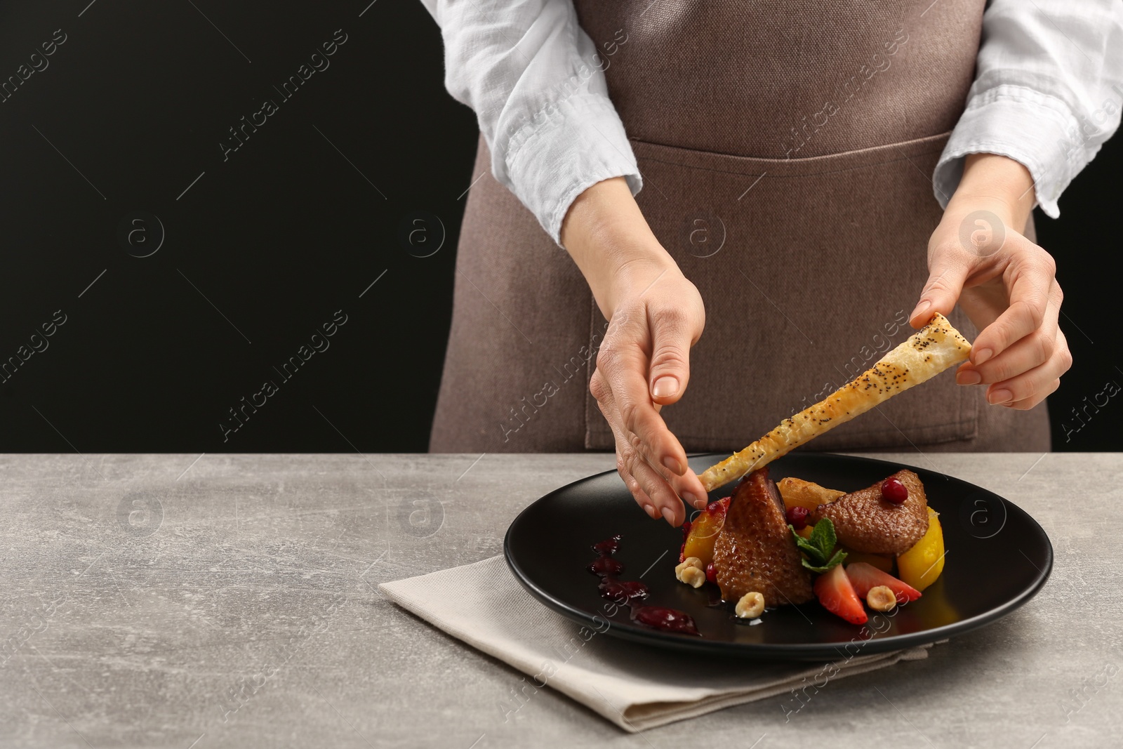 Photo of Food stylist preparing delicious dish with chicken, parsnip and strawberries for photoshoot at grey table in studio, closeup. Space for text