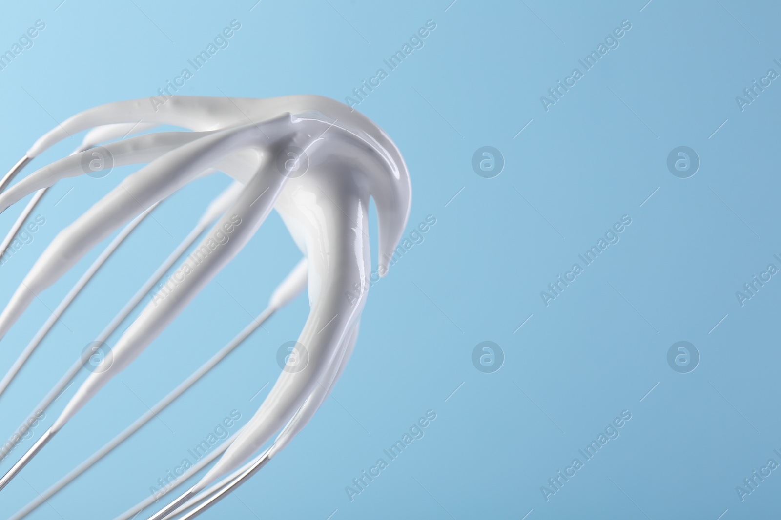 Photo of Whisk with whipped cream on light blue background, closeup. Space for text