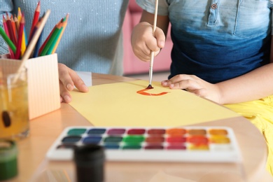 Photo of Cute little child painting at table with his mother, closeup. Playing room